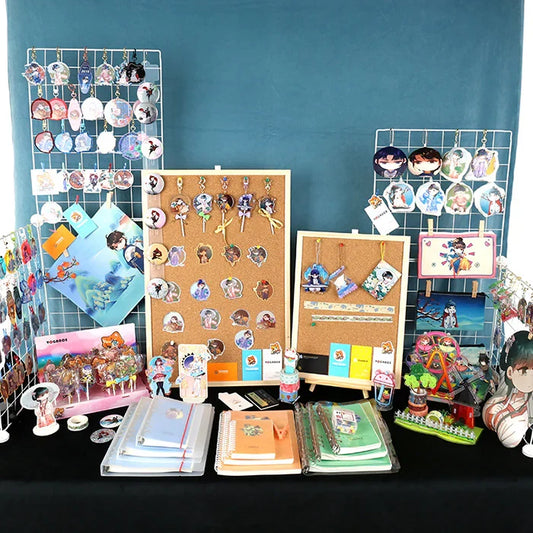 Anime keychains, acrylic charms, standees, stickers, and notebooks displayed on tables and racks